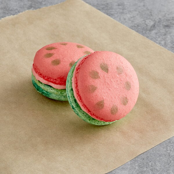 Two Macaron Centrale watermelon macarons on a piece of paper.