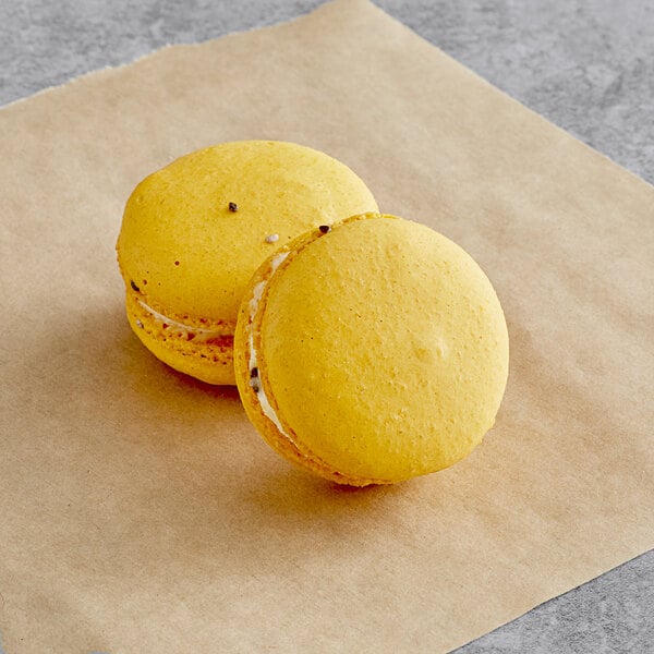 Two yellow Passion Fruit macarons on a piece of brown paper.