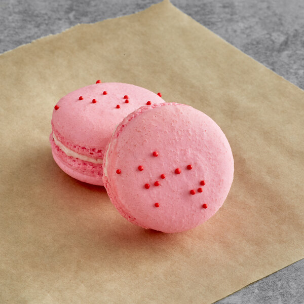 Two pink Macaron Centrale pomegranate macarons on brown paper.