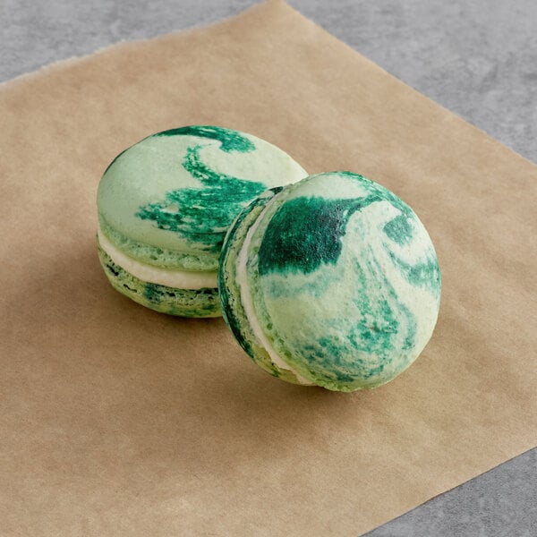 Two green and white Macaron Centrale Pina Colada macarons on a brown paper.