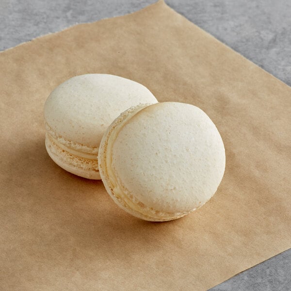 Two vanilla macarons on brown paper.