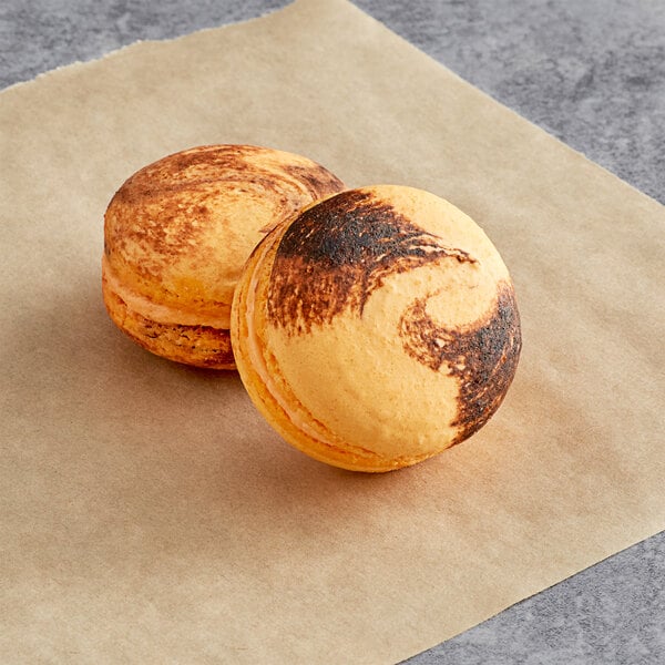 Two Macaron Centrale Thai tea macarons on a paper with brown and orange swirls.