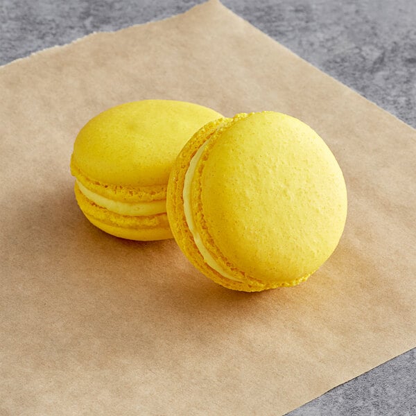 Two yellow Macaron Centrale lemon macarons on brown paper.