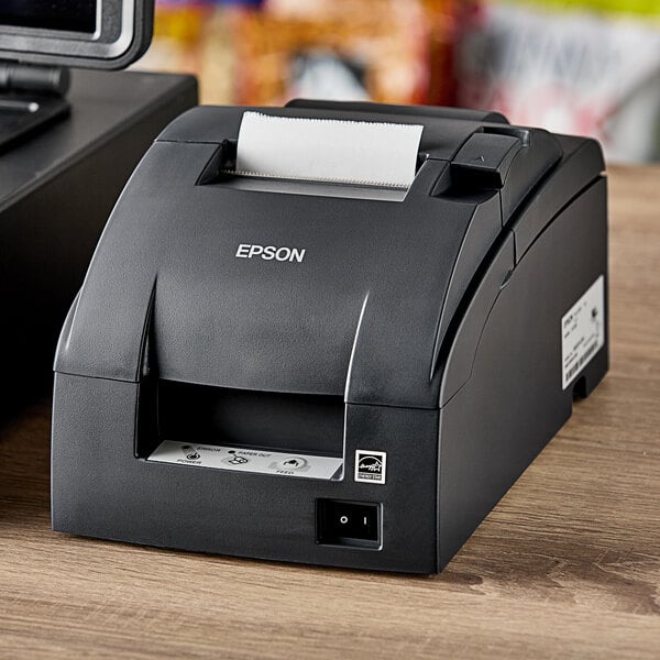 An Epson TM-U220B receipt printer on a table with a paper roll inside.