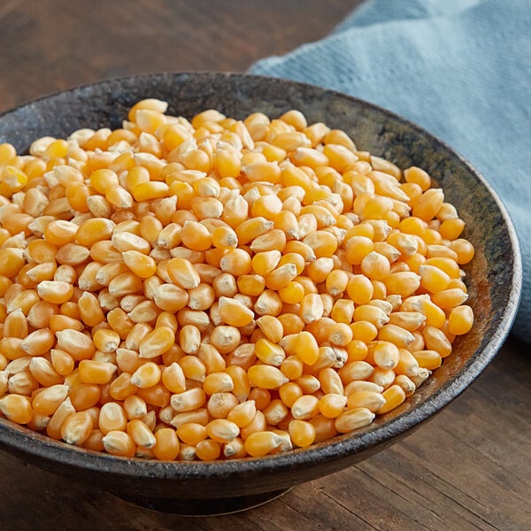 A bowl of Pop Weaver Gold Butterfly popcorn kernels on a blue cloth.