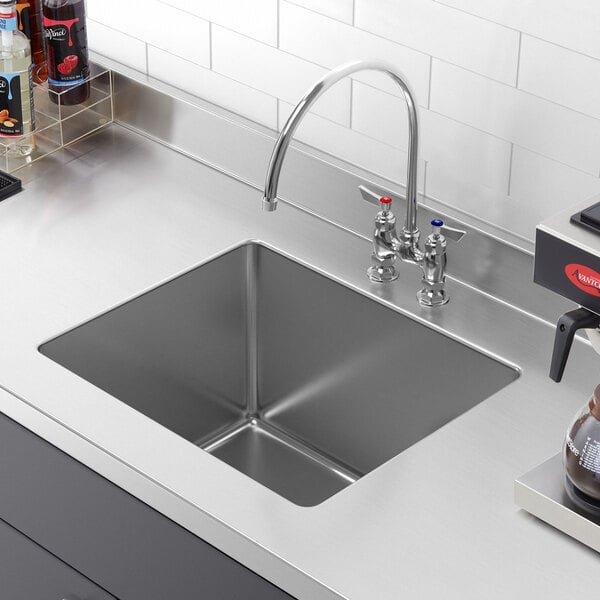 A close-up of a Regency stainless steel weld-in sink bowl with a faucet and coffee maker on the counter.