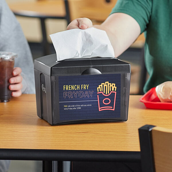 A person using a black Choice tabletop napkin dispenser to get a napkin.