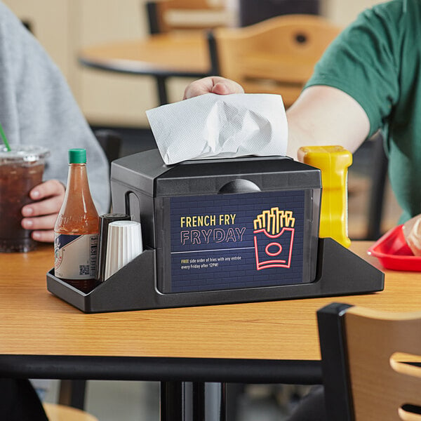 A Choice tabletop napkin dispenser with a napkin and condiments on a table.