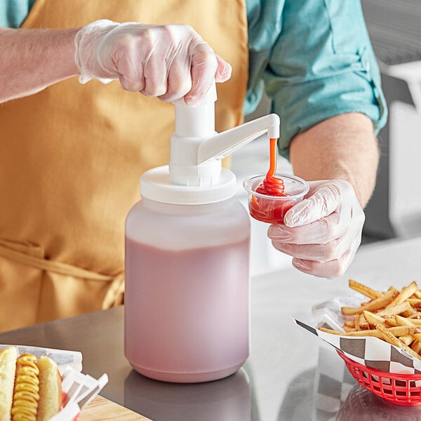 A person using a Choice plastic condiment pump to pour red liquid into a cup.