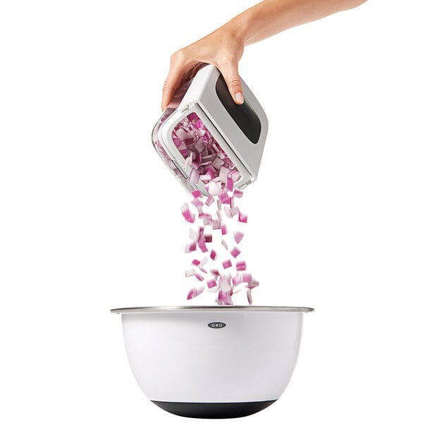 A hand using the OXO Manual Vegetable Chopper to chop onions into a white and black pot.