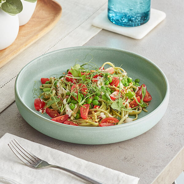 A bowl of Acopa Pangea Harbor Blue Porcelain pasta with tomatoes, peas, and sprouts.