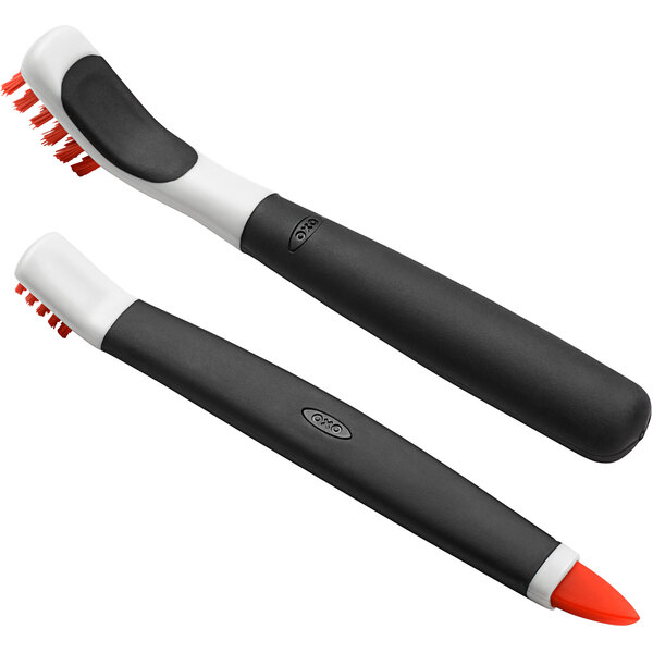 An OXO Good Grips janitorial brush set with orange handles and black bristles.