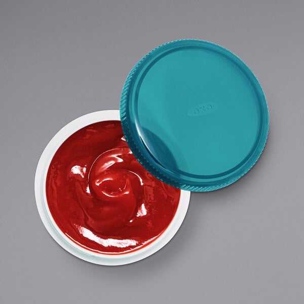 An OXO Prep & Go container with a blue lid filled with red sauce.