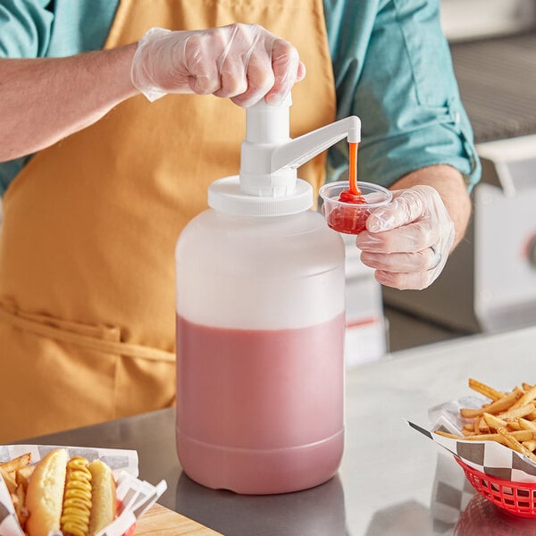 A person using a Choice plastic condiment pump to pour pink liquid into a container.