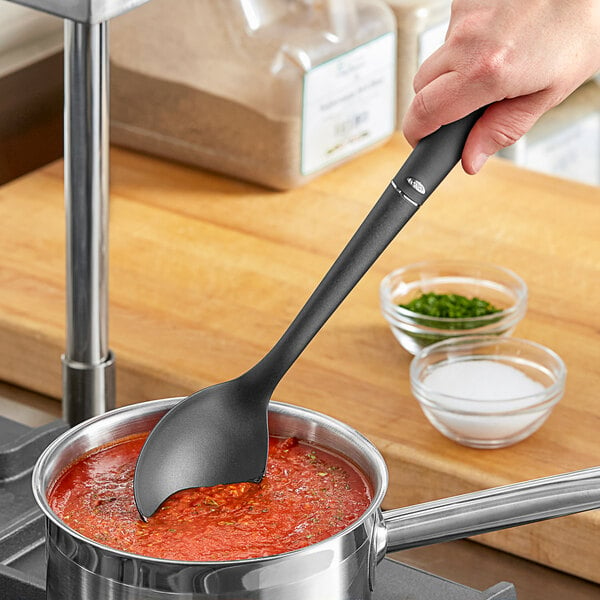 A person using an OXO Good Grips high heat nylon solid spoon to stir red sauce in a pot.