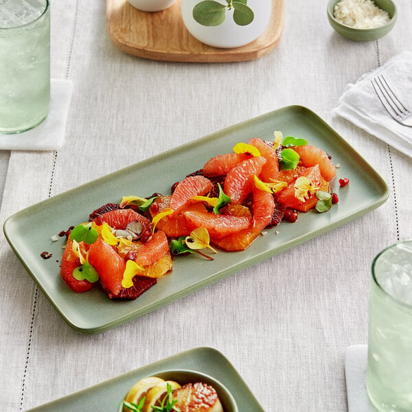 An Acopa sage rectangular porcelain platter with a salad and a glass of water on a table.