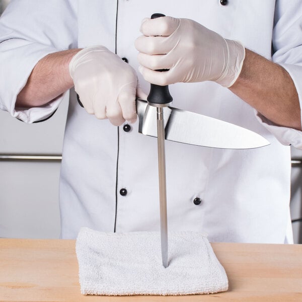Man drawing chef knife downward on a vertical sharpening steel on top of a bar towel
