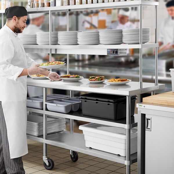 A chef in a white coat standing by a Regency stainless steel table with food on it.