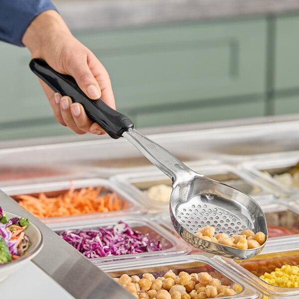 A hand holding a black Vollrath Spoodle over a tray of food.