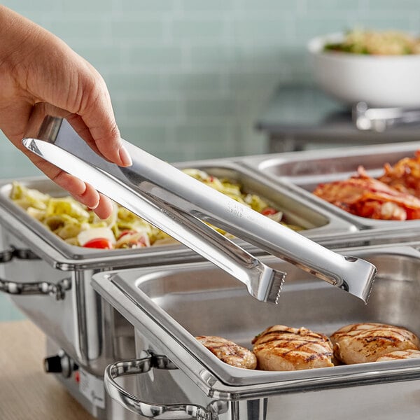 A person using Vollrath metal tongs to serve food at a buffet.