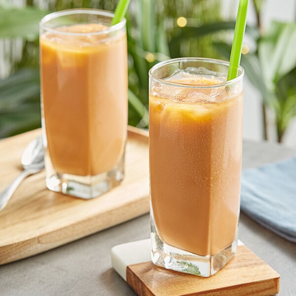 Two glasses of Fanale Thai tea with green straws on a table.