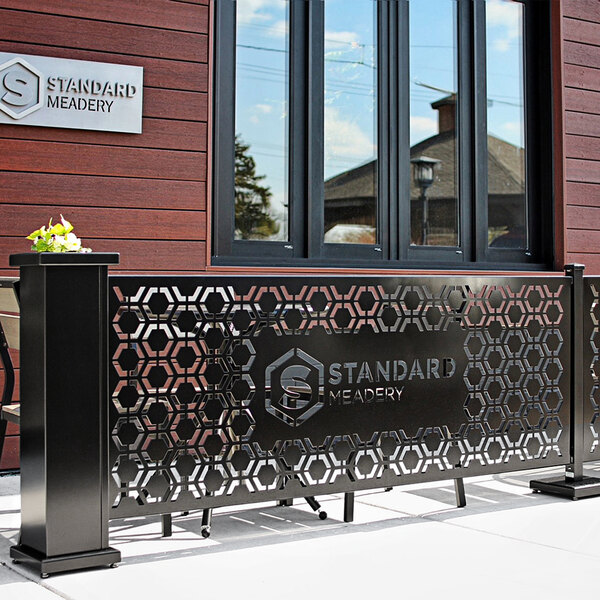 A black metal SelectSpace hexagonal pattern partition panel on an outdoor patio with a flower pot on the side.