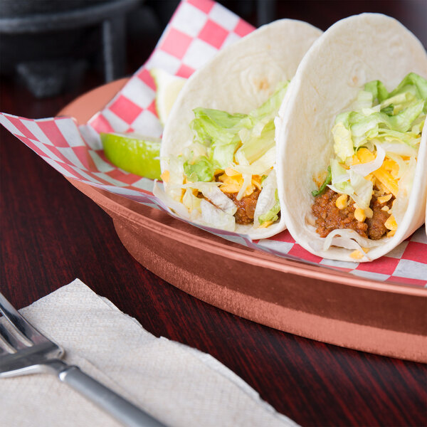 A paprika oval deli server with tacos on it on a table in a Mexican restaurant.