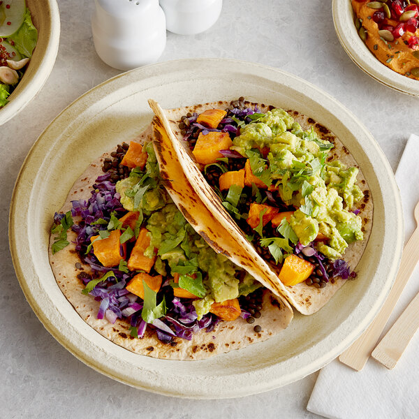 A Tellus Products bagasse plate with two tacos and a salad on it.