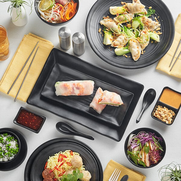 A table with Acopa Izumi matte black melamine bowls filled with food.