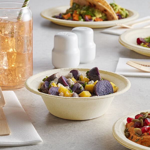A Tellus natural bagasse bowl of food on a table with a plate of food and a glass of liquid.