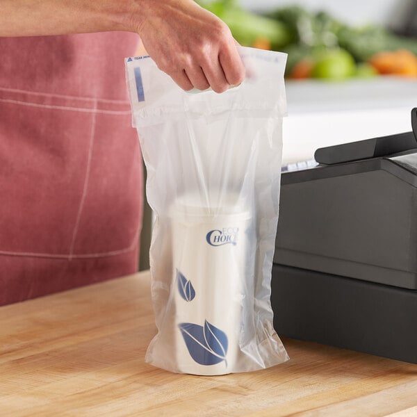 A person's hand holding a Fast Take clear plastic drink carrier on a counter.