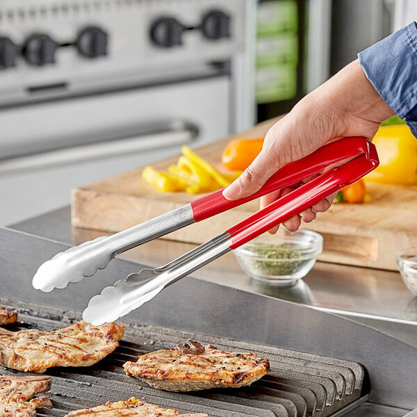 A person using Vollrath stainless steel tongs with a red handle to serve food