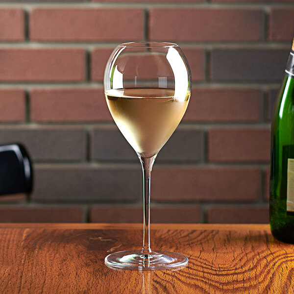 An Anchor Hocking white wine glass filled with white wine next to a bottle of white wine on a table.