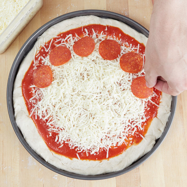 A person putting pepperoni on an American Metalcraft hard coat anodized aluminum pizza pan.
