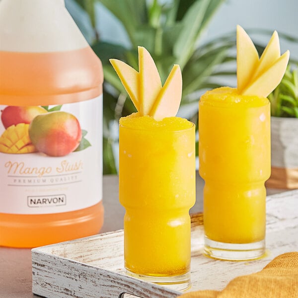 Two glasses of yellow Narvon mango slushies with fruit on the rim.