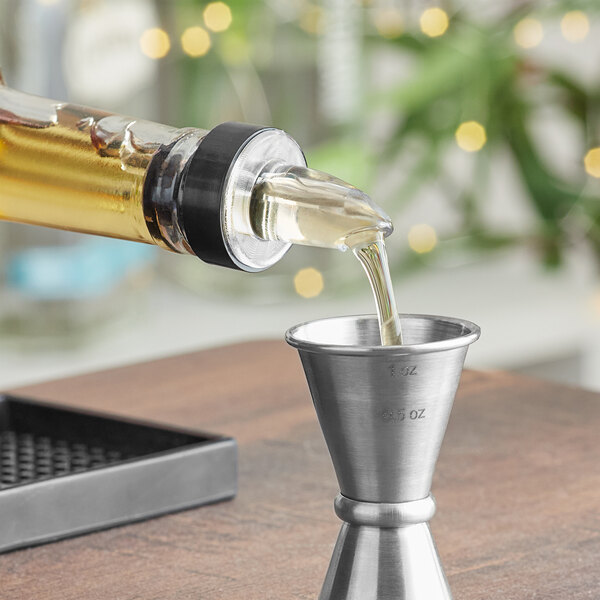 A person using a Franmara Crystal Fast Flow Pourer to pour liquid into a metal cup.