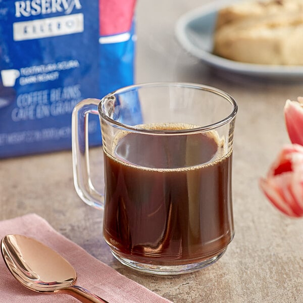 A glass mug of Lavazza whole bean coffee with a spoon.