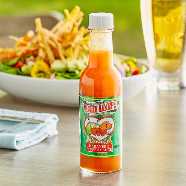 A bottle of Marie Sharp's Mild Habanero hot sauce on a table next to a bowl of salad.