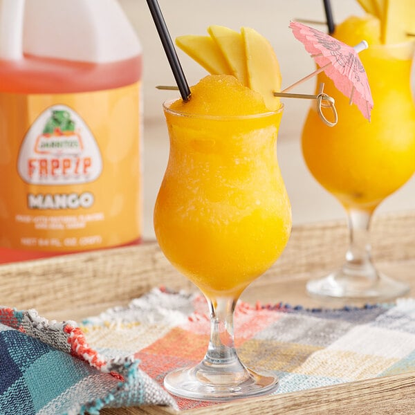 A glass of mango slushy next to a Jarritos Mango Slushy Concentrate container.