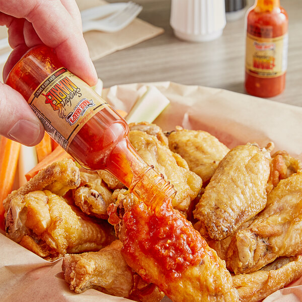 A hand pouring Marie Sharp's Smokin' Marie Habanero hot sauce onto a chicken wing.