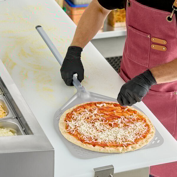 A square perforated aluminum pizza peel with a long handle being used to prepare a pizza.