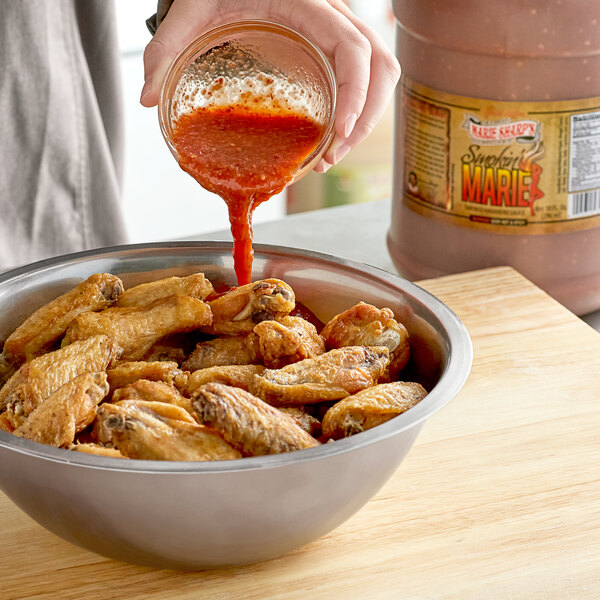 A person pouring Smokin' Marie hot sauce into a bowl of chicken wings.