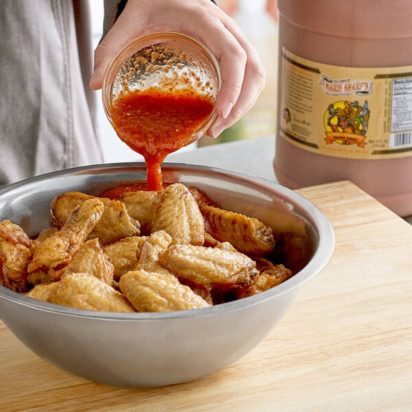 A person pouring Marie Sharp's Smoked Habanero Hot Sauce into a bowl of chicken wings.