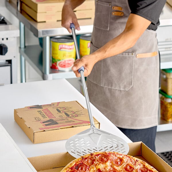 A round stainless steel perforated pizza peel with a long handle being used to serve a pepperoni pizza.
