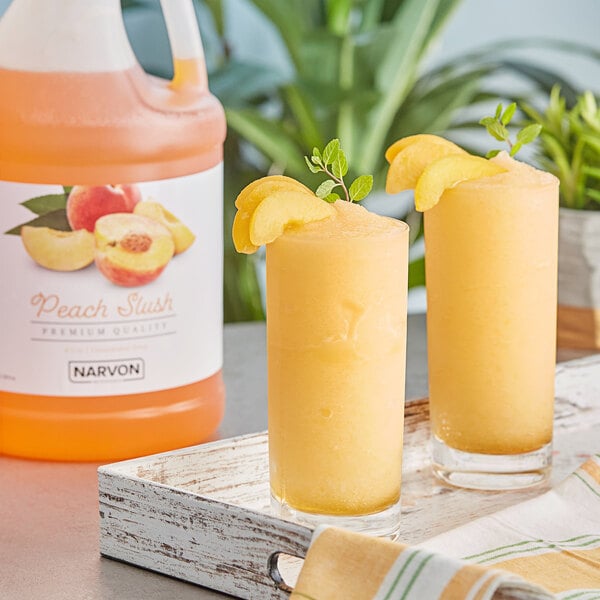 A pitcher of Narvon Peach Slushy made with Narvon Peach Slushy concentrate on a table with glasses of peach slushies.