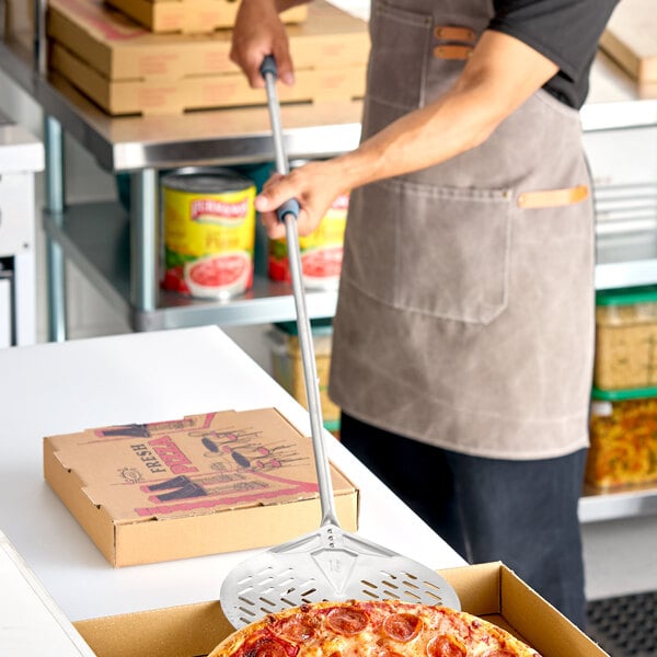 A round perforated stainless steel pizza peel with a long handle being used to transfer a pizza.