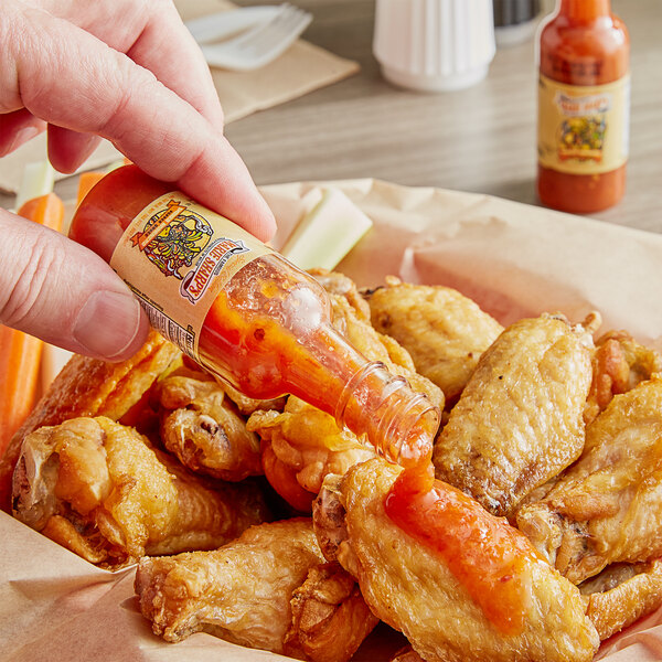 a hand pouring hot sauce into a hot dog