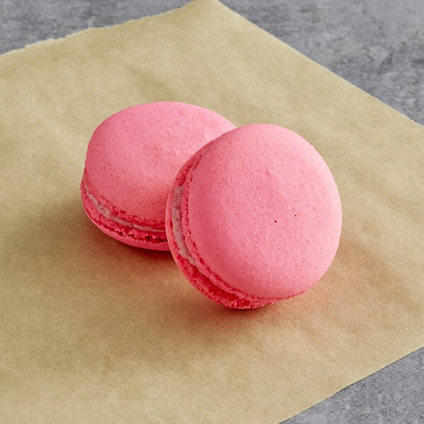 Two Macaron Centrale raspberry macarons on brown paper.