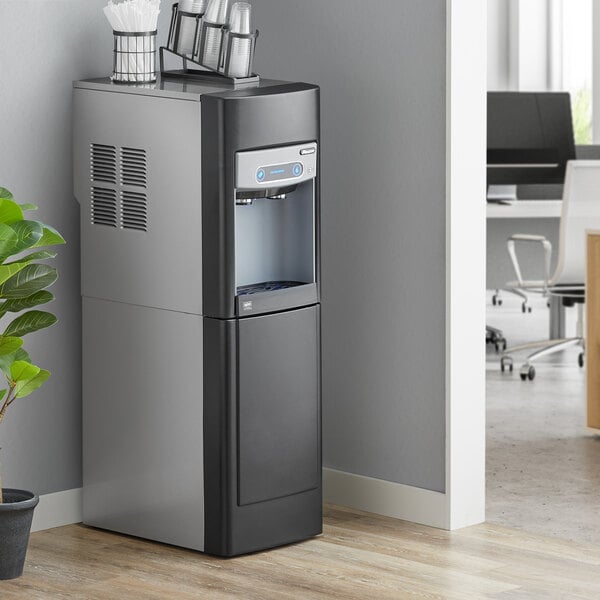 A Follett air cooled Chewblet ice maker and water dispenser with a stand and filter in a corporate office cafeteria.