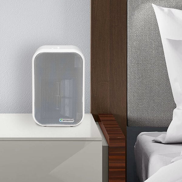 A white and gray Guardian Technologies air purifier on a white countertop next to a bed.